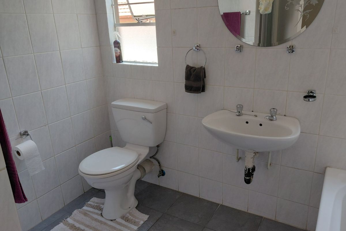 A functional bathroom featuring tiled walls and flooring, a wall-mounted basin, and a standard toilet, offering a clean and practical layout.