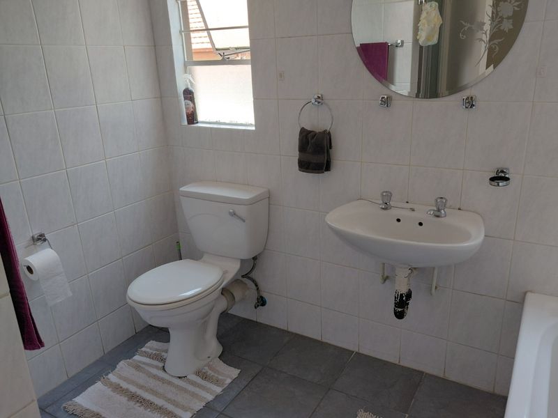 A functional bathroom featuring tiled walls and flooring, a wall-mounted basin, and a standard toilet, offering a clean and practical layout.