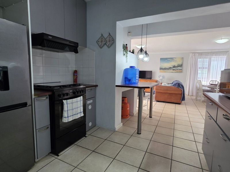 Open-plan kitchen and living area featuring tiled flooring, built-in cabinetry, and a breakfast bar, creating a functional and connected living space.