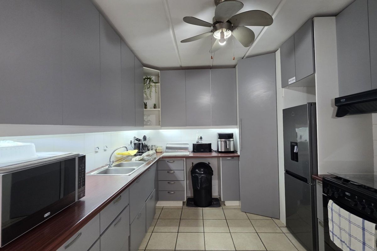 A functional kitchen featuring modern grey cabinetry, laminate countertops, a double bowl sink, and tiled flooring with an integrated extractor fan.