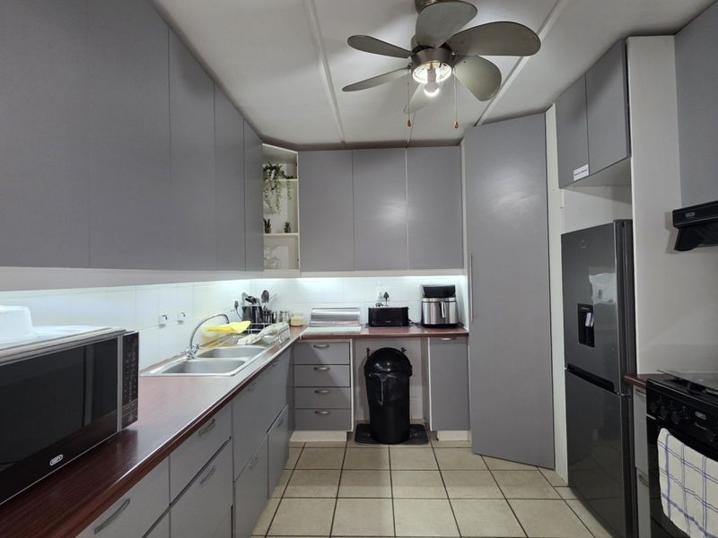 A functional kitchen featuring modern grey cabinetry, laminate countertops, a double bowl sink, and tiled flooring with an integrated extractor fan.