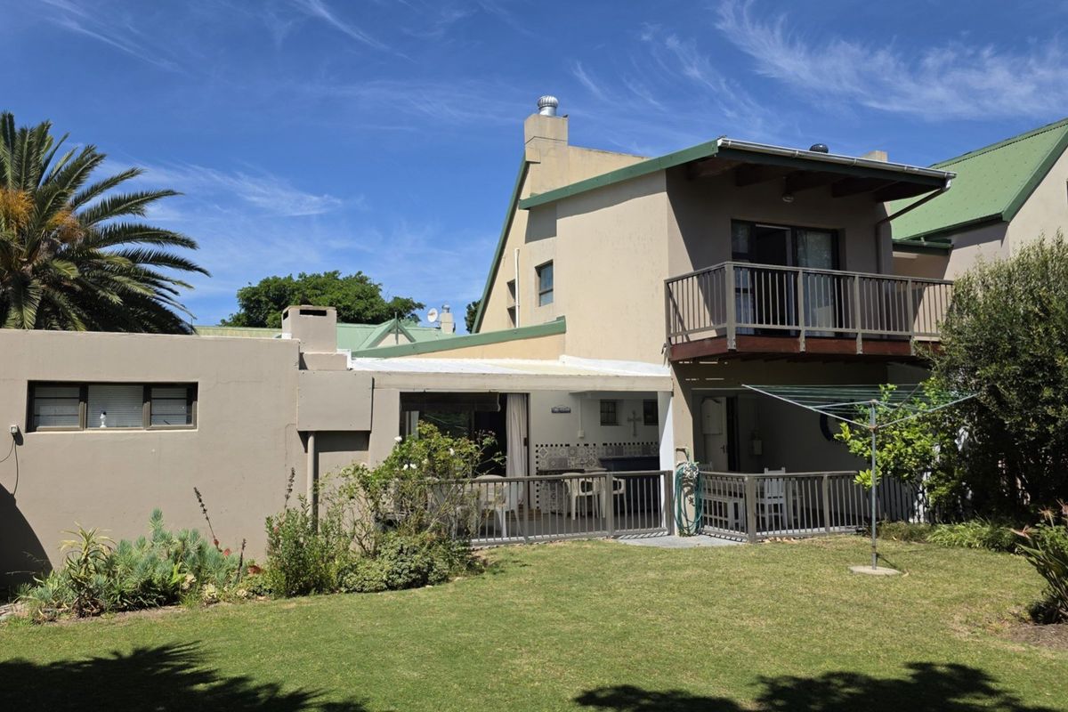 Rear view of the house featuring a covered patio, an upper-level balcony, and a landscaped garden area with a rainwater tank.