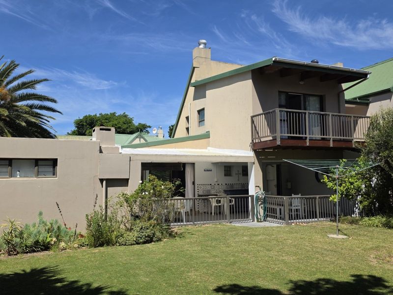 Rear view of the house featuring a covered patio, an upper-level balcony, and a landscaped garden area with a rainwater tank.