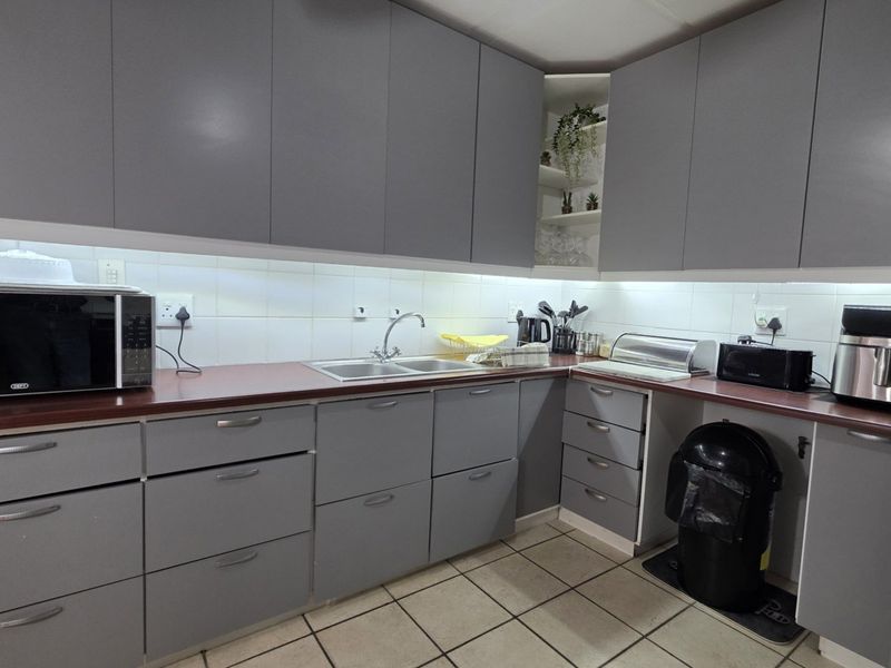A functional kitchen featuring modern grey cabinetry, a dark laminate countertop, double basin sink, and tiled backsplash with integrated under-cabinet lighting.