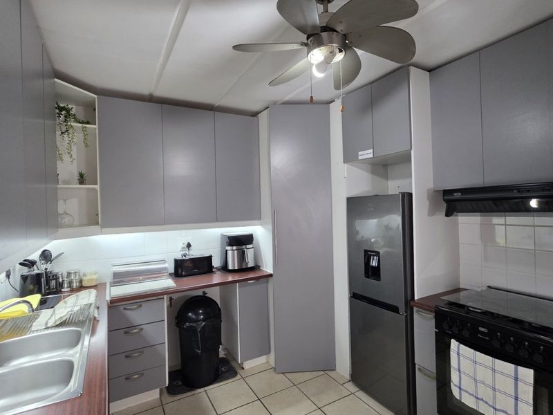 A functional kitchen featuring grey built-in cabinetry, laminate countertops, a double bowl sink, and tiled flooring with a ceiling fan.