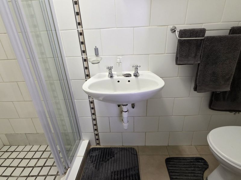 A functional bathroom featuring a wall-mounted basin, a shower enclosure with glass doors, and tiled wall finishes.
