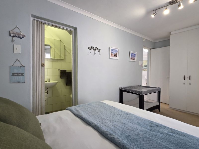A bedroom featuring a built-in wardrobe, track lighting, and an en-suite bathroom accessed via a folding door.