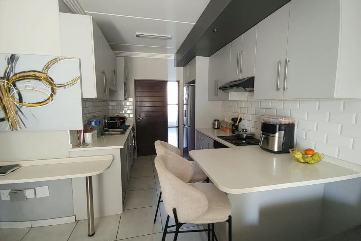 Modern kitchen featuring sleek cabinetry, subway tile backsplash, stone countertops, and a functional breakfast bar area with tiled flooring.