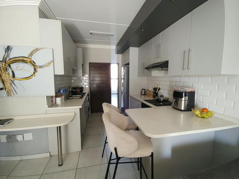 Modern kitchen featuring sleek cabinetry, subway tile backsplash, stone countertops, and a functional breakfast bar area with tiled flooring.