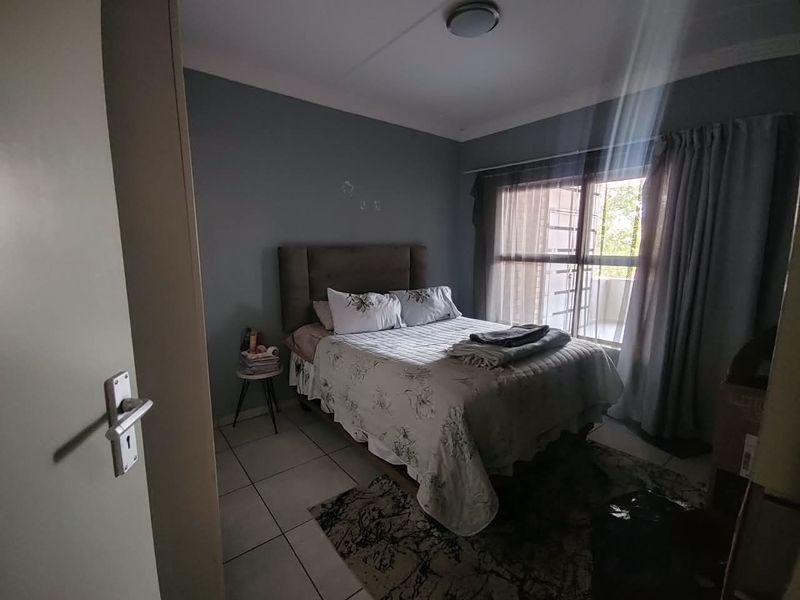 A functional bedroom featuring tiled flooring and a sliding door providing access to an outdoor area, with neutral wall finishes.