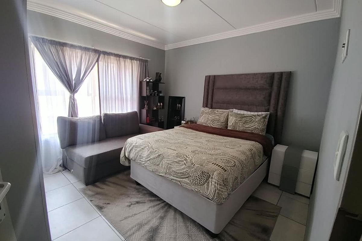 A well-lit bedroom featuring neutral grey walls, tiled flooring, and decorative ceiling cornicing, providing a comfortable and functional living space.