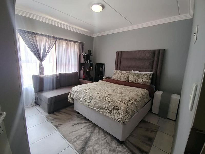 A well-lit bedroom featuring neutral grey walls, tiled flooring, and decorative ceiling cornicing, providing a comfortable and functional living space.