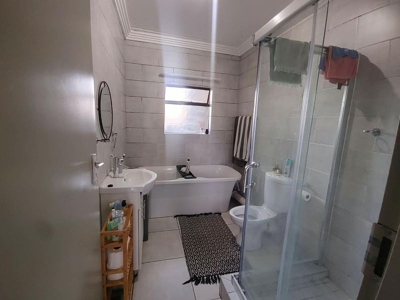A well-maintained bathroom featuring a freestanding bathtub, a separate glass-enclosed shower, a pedestal washbasin, and neutral wall tiling.