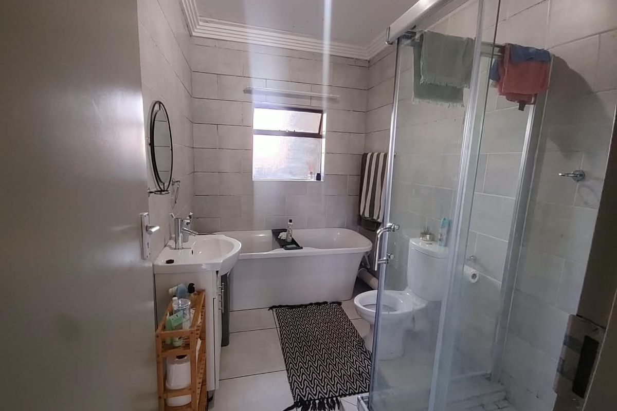 A functional bathroom featuring a freestanding bathtub, a separate glass-enclosed shower, a pedestal washbasin, and neutral ceramic wall and floor tiling.