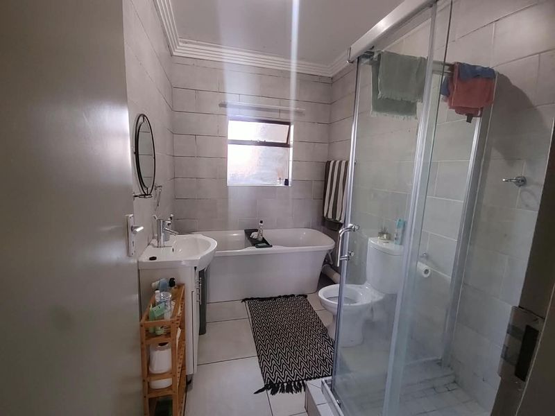 A functional bathroom featuring a freestanding bathtub, a separate glass-enclosed shower, a pedestal washbasin, and neutral ceramic wall and floor tiling.
