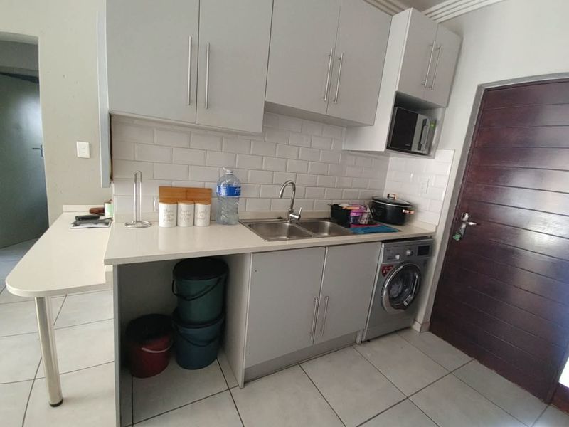 A compact kitchen featuring modern grey cabinetry, subway tile backsplash, stone countertops, a double sink, and an integrated washing machine.