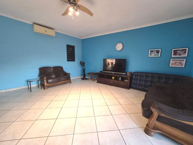 Spacious living room featuring tiled flooring, a ceiling fan, and a wall-mounted air conditioning unit.