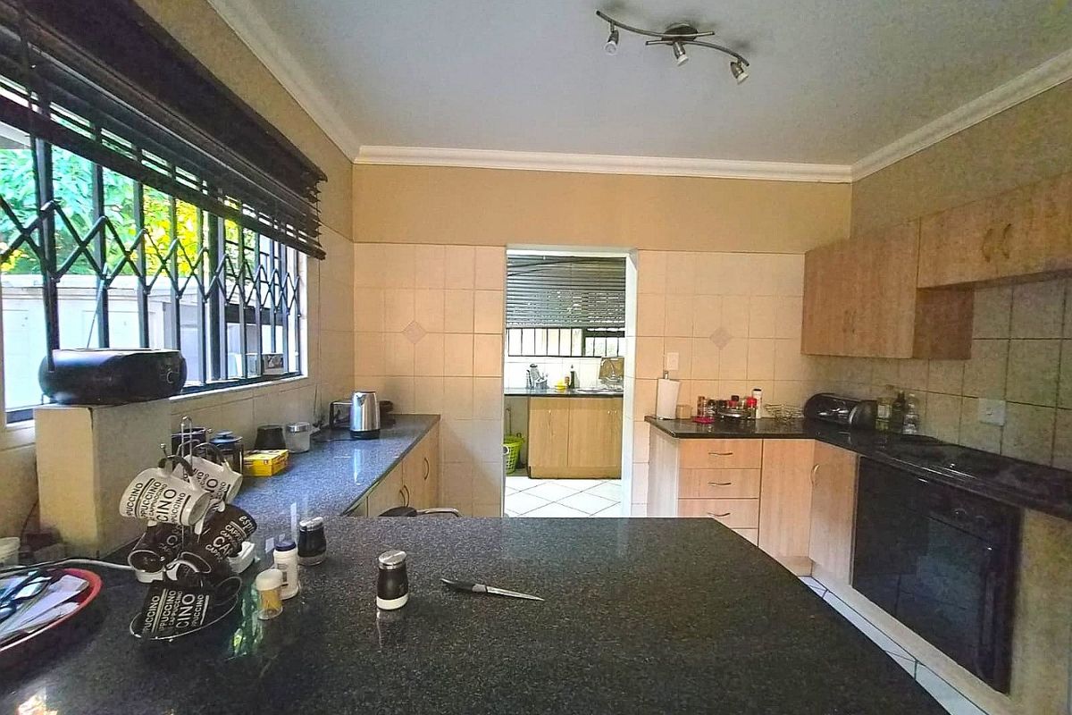 Functional kitchen featuring granite countertops, built-in oven, hob, and ample cabinetry, with an adjoining scullery area visible through the doorway.