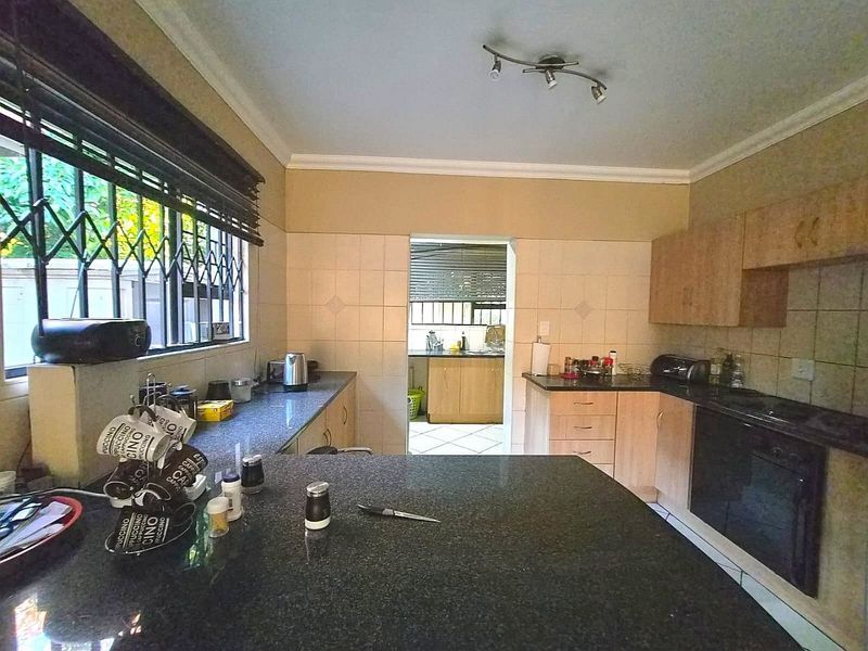 Functional kitchen featuring granite countertops, built-in oven, hob, and ample cabinetry, with an adjoining scullery area visible through the doorway.
