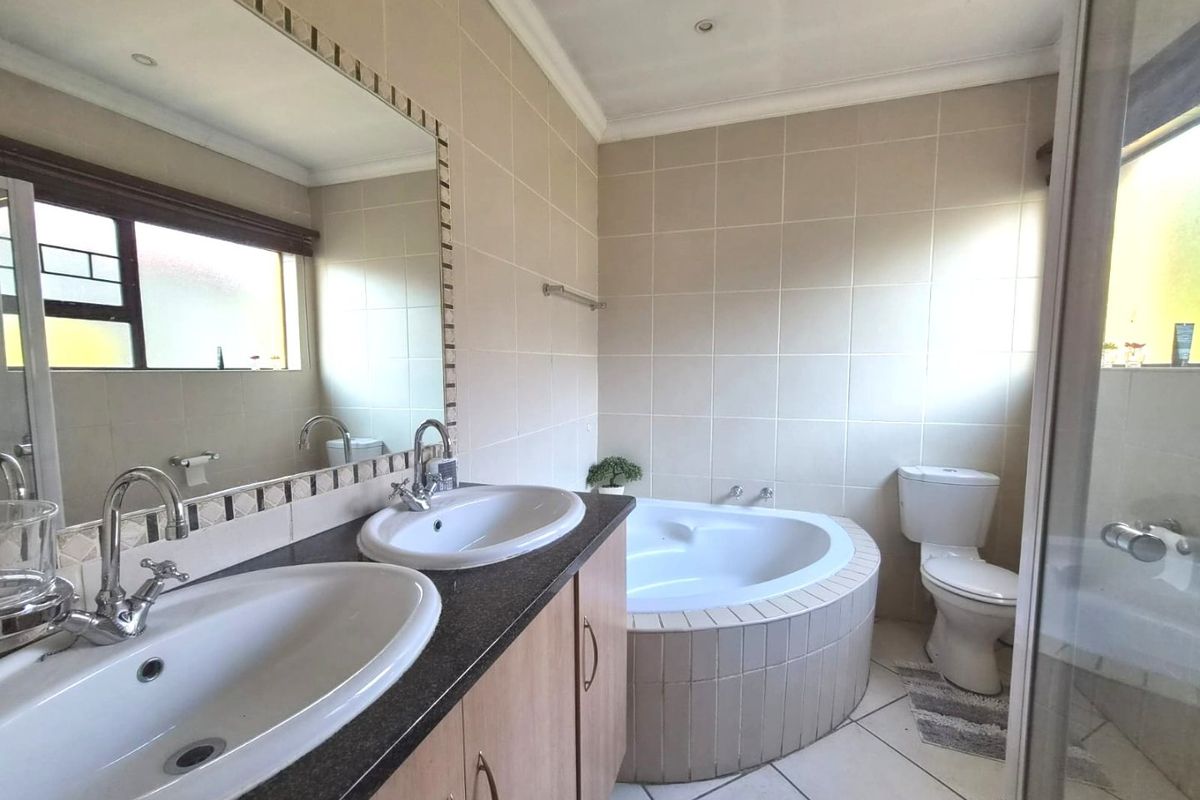 A functional bathroom featuring a double vanity, built-in corner bathtub, toilet, and a separate shower enclosure with neutral wall and floor tiling.