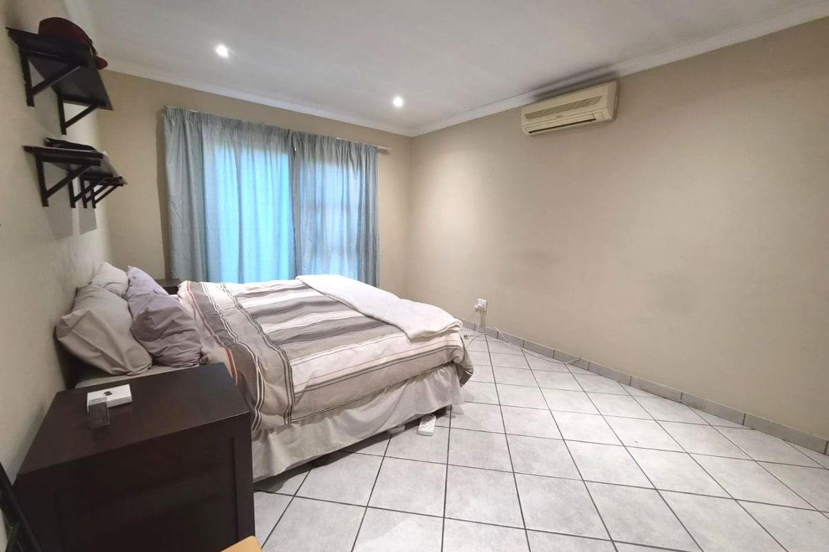 A spacious bedroom featuring tiled flooring, recessed lighting, and a wall-mounted air conditioning unit, with access to a sliding glass door.
