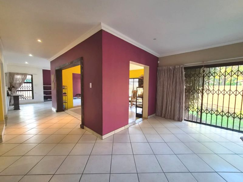 Spacious open-plan living area featuring ceramic floor tiles, recessed lighting, and large sliding glass doors with security gates leading to the garden.