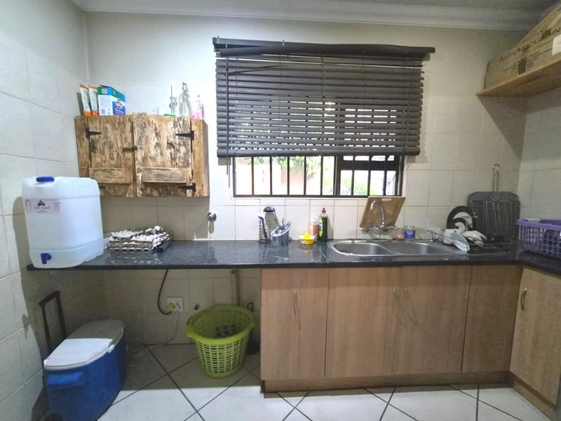 A functional scullery area featuring granite countertops, double sink, tiled backsplash, and laminate cabinetry with a window overlooking the exterior.