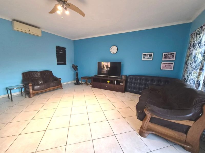 A spacious living room featuring tiled flooring, a ceiling fan, and a wall-mounted split-system air conditioner.