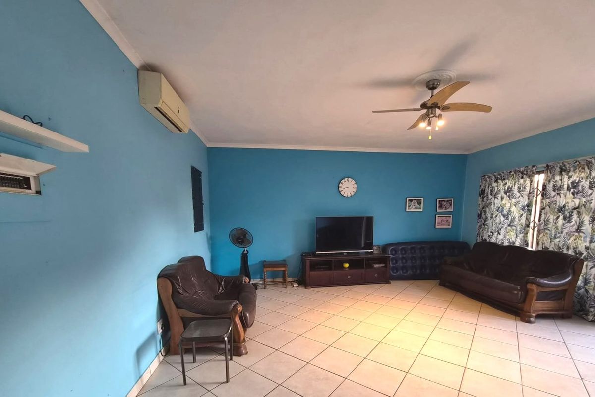 A spacious living room featuring tiled flooring, a ceiling fan, and a wall-mounted air conditioning unit.