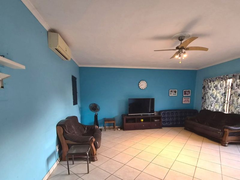 A spacious living room featuring tiled flooring, a ceiling fan, and a wall-mounted air conditioning unit.