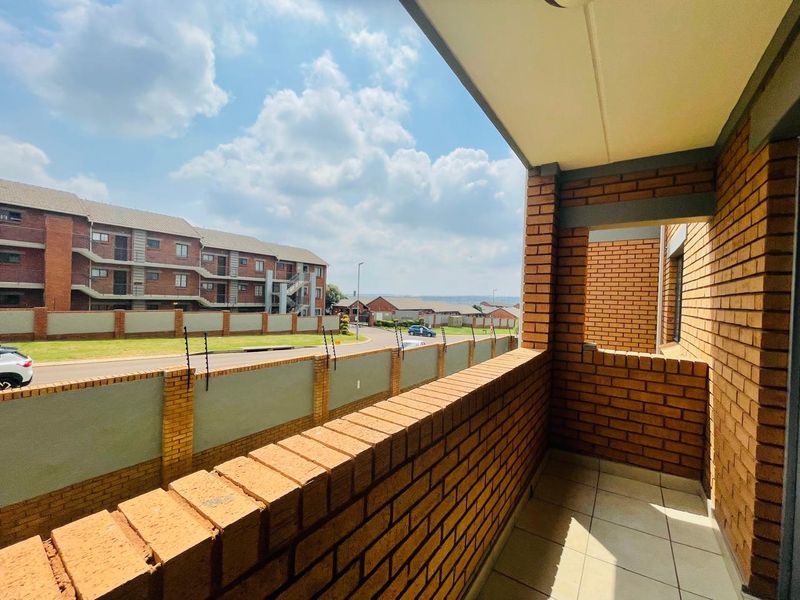 A covered balcony featuring a brick balustrade and tiled flooring, offering an elevated view of the surrounding residential complex and street.