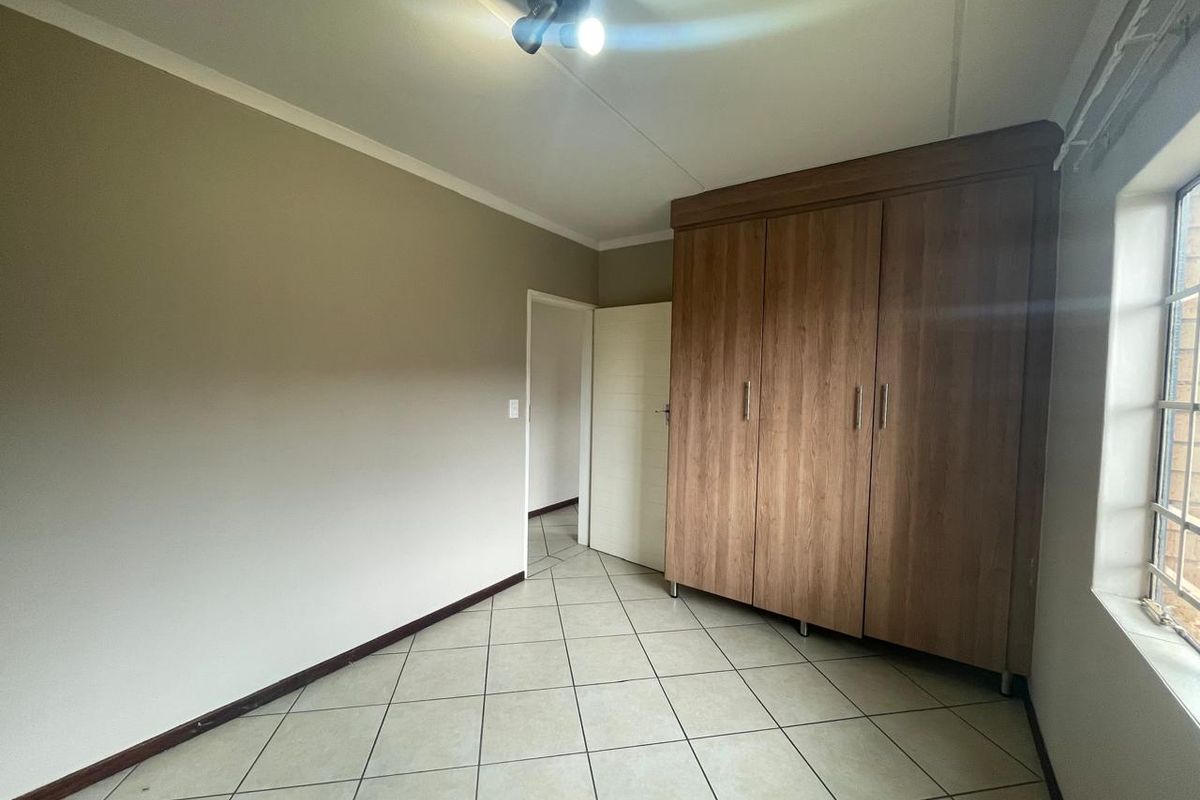 A clean, empty bedroom featuring neutral wall tones, tiled flooring, and ample built-in wooden cupboards, offering a versatile space ready for personalization.