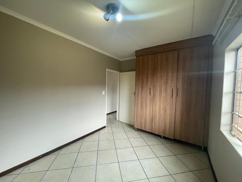 A clean, empty bedroom featuring neutral wall tones, tiled flooring, and ample built-in wooden cupboards, offering a versatile space ready for personalization.