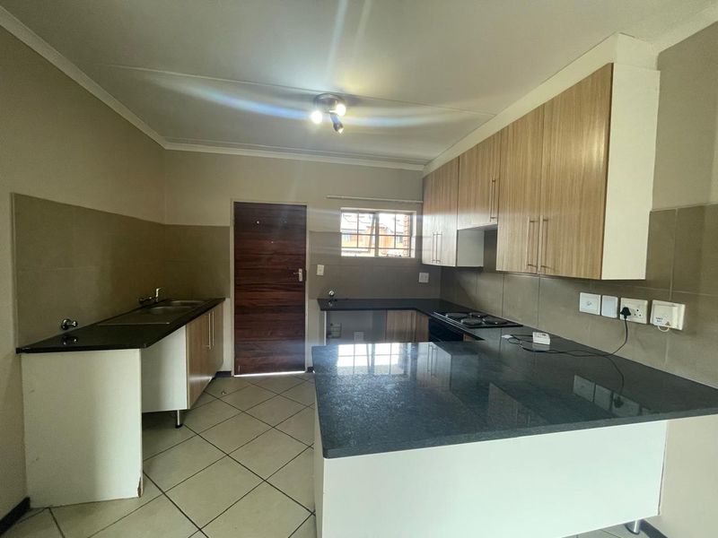 A clean, functional kitchen featuring modern wood-finish cabinetry, dark granite countertops, a built-in electric hob, and tiled flooring.