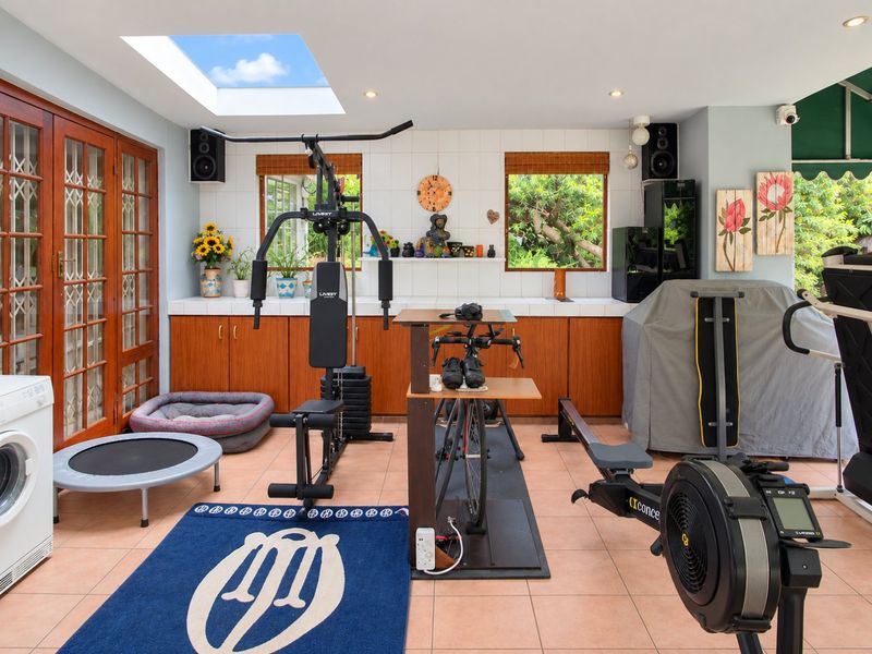 A well-lit home gym featuring tiled flooring, built-in cabinetry with a tiled splashback, and a skylight, providing a functional space for fitness activities.