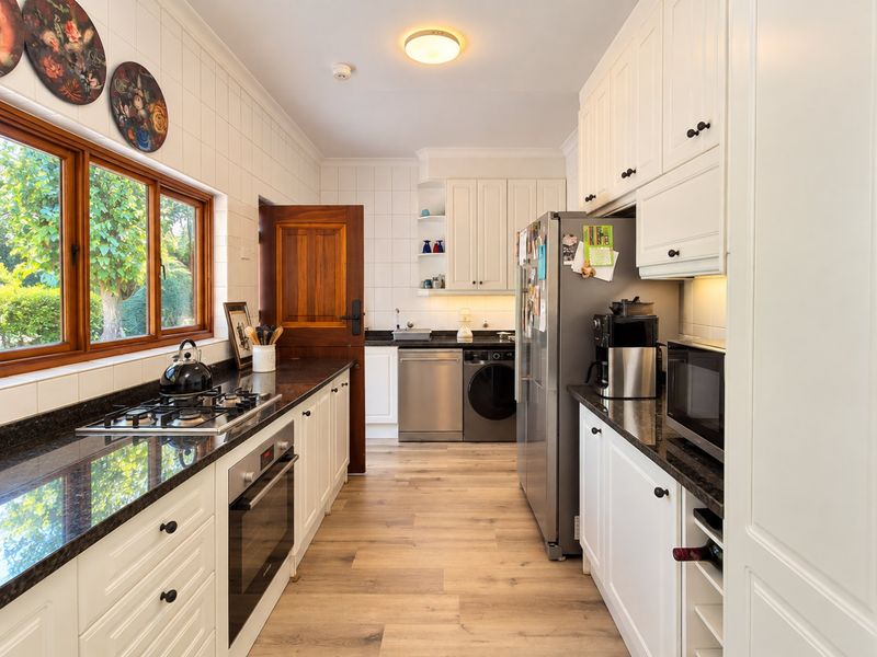 A well-maintained kitchen featuring white cabinetry, granite countertops, a gas hob, built-in oven, and integrated dishwasher with timber accents.