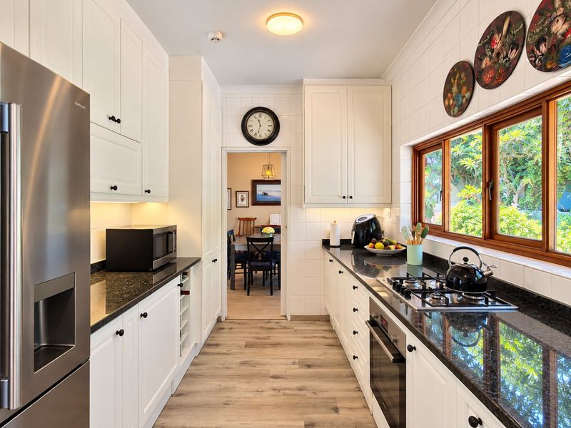 A well-maintained galley kitchen featuring white shaker-style cabinetry, dark granite countertops, a built-in oven, gas hob, and light wood-look laminate flooring.