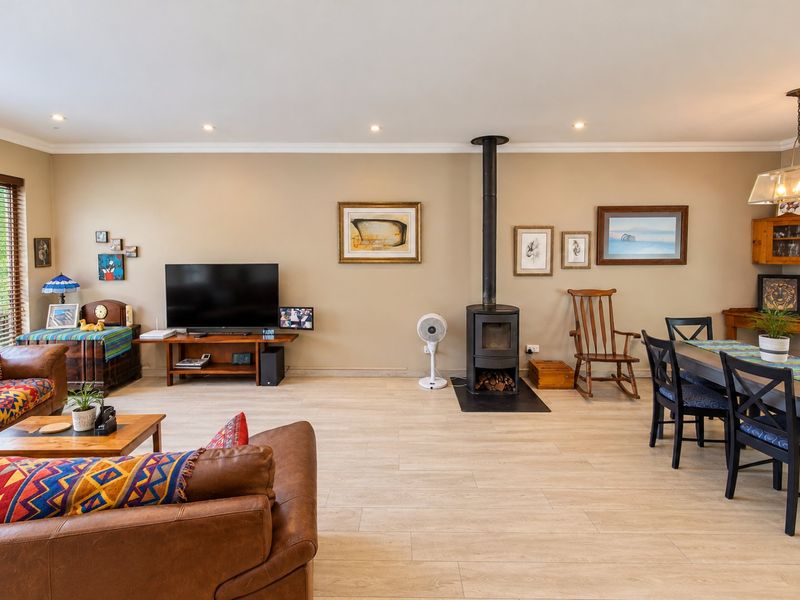 Spacious open-plan living and dining area featuring a central wood-burning stove, recessed lighting, and modern timber-look tile flooring.