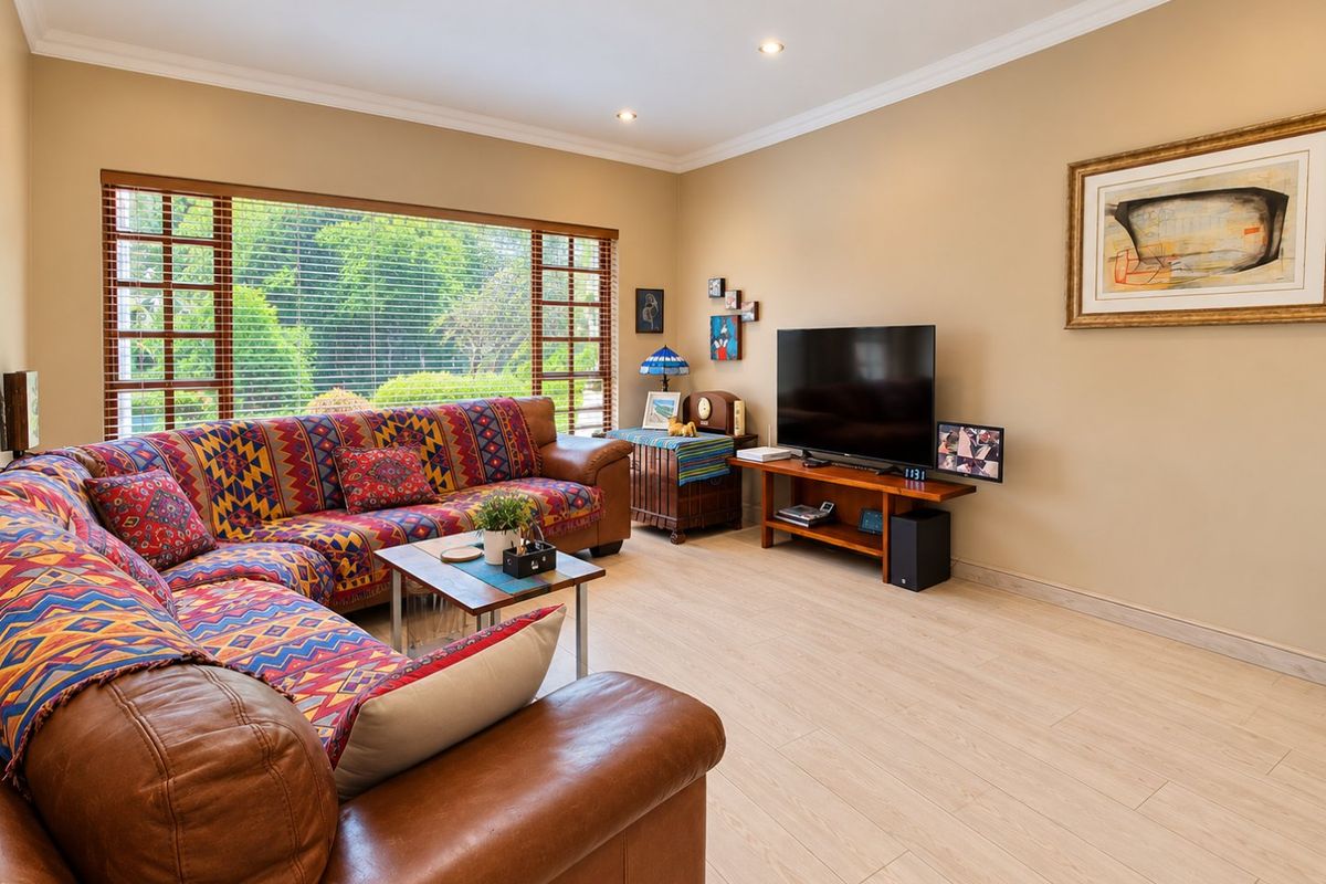 A well-maintained living room featuring light timber-look tile flooring, recessed downlighting, and a large window providing natural light and garden views.