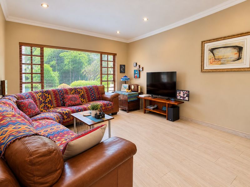 A well-maintained living room featuring light timber-look tile flooring, recessed downlighting, and a large window providing natural light and garden views.