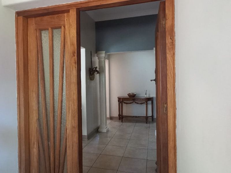 A view through a wooden framed glass door into a tiled hallway featuring a decorative column and neutral wall finishes.