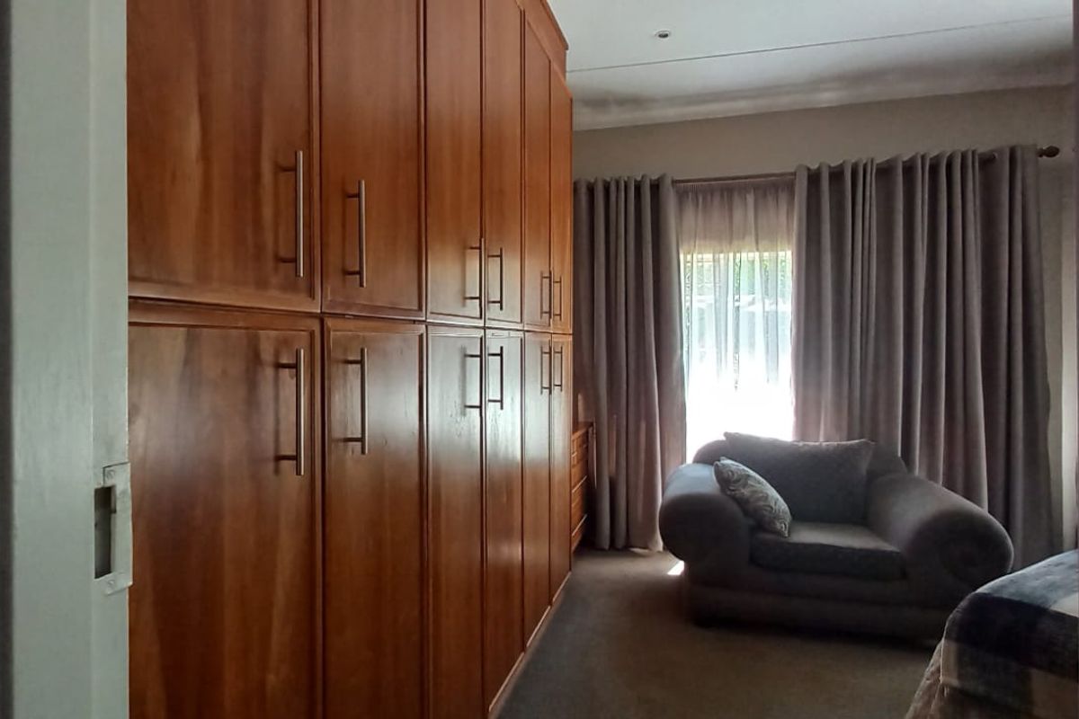 A bedroom featuring extensive floor-to-ceiling built-in wooden cupboards and neutral window treatments.
