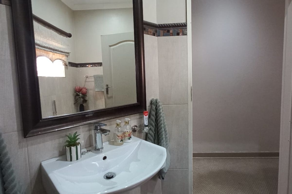 A functional bathroom featuring a wall-mounted basin with a chrome mixer tap, a framed mirror, and decorative tiled wall accents.