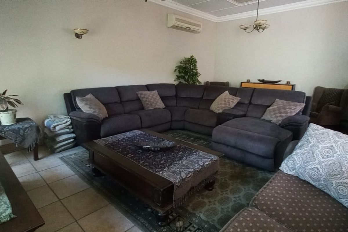 A spacious living room featuring tiled flooring, coved cornicing, and a wall-mounted air conditioning unit.