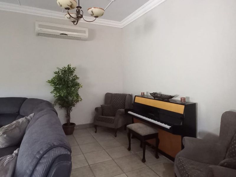 A spacious living room featuring tiled flooring, decorative ceiling cornicing, and a wall-mounted split-system air conditioning unit.