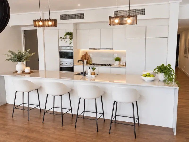 Modern kitchen featuring a large stone island, integrated appliances, sleek white cabinetry, and recessed ducted air conditioning in an open-plan layout.