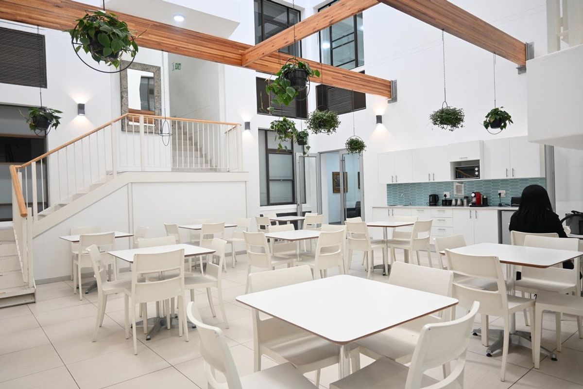 Spacious open-plan commercial area featuring a modern kitchenette, tiled flooring, exposed wooden beams, and a staircase leading to an upper level.