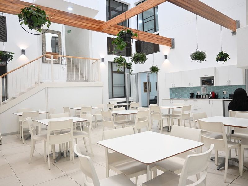 Spacious open-plan commercial area featuring a modern kitchenette, tiled flooring, exposed wooden beams, and a staircase leading to an upper level.