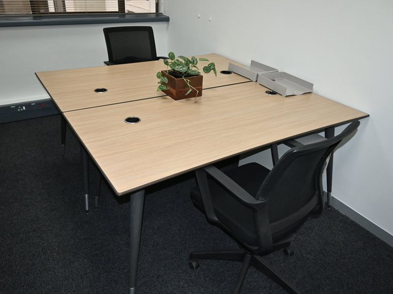 A functional office space featuring carpeted flooring, integrated power and data points, and window blinds, suitable for a professional work environment.