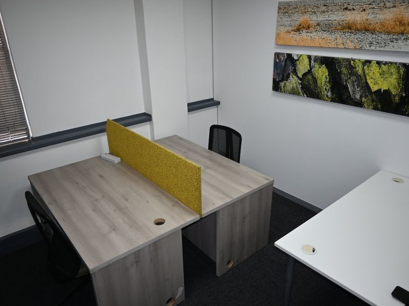 A functional commercial office space featuring neutral walls, carpeted flooring, and venetian blinds, providing a clean and professional work environment.